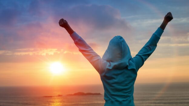 Person in blue hoodie doing a victory post in front of a sunrise